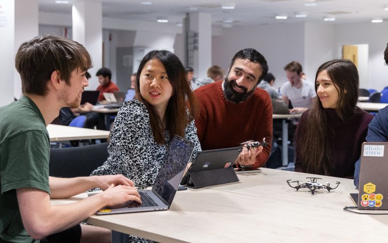 A group of people engaged in a group projected, seated around a table with multiple laptops.