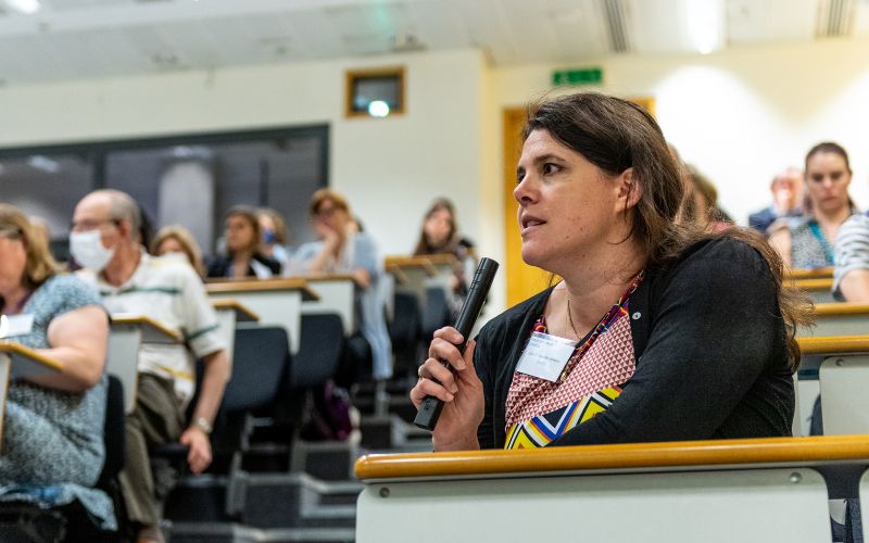 A woman asking a question using a handheld microphone, in the middle of a full lecture theatre.