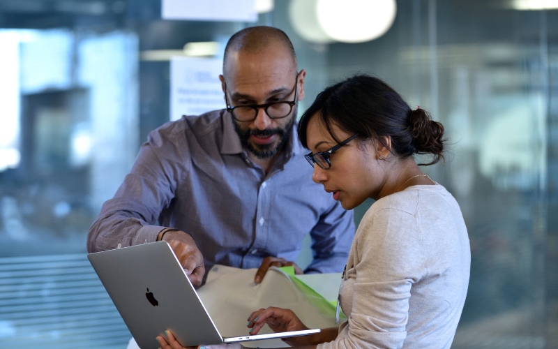 Two people working on a group project, both looking at a laptop screen.