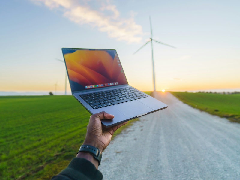A person is holding a laptop in the middle of a road in front of a wind turbine.