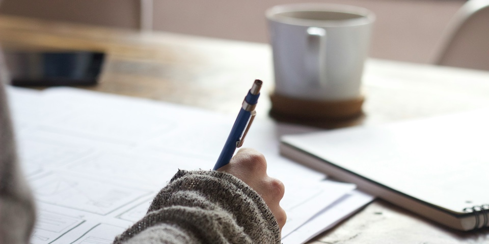 Hand writing in a notebook on a desk.